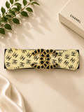 Chanel headband with logo pattern on a beige surface with a Chanel box in the background.