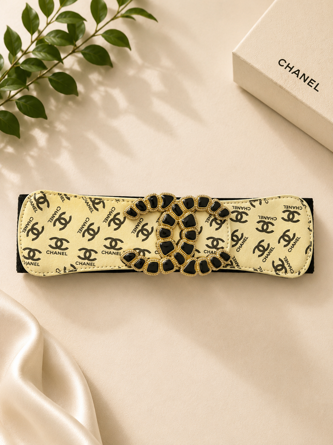 Chanel headband with logo pattern on a beige surface with a Chanel box in the background.